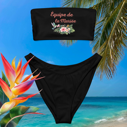 Bikini bandeau noir avec inscription Équipe de la Mariée et fleurs tropicales présenté sur décor plage exotique, idéal pour EVJF et vacances d’été.