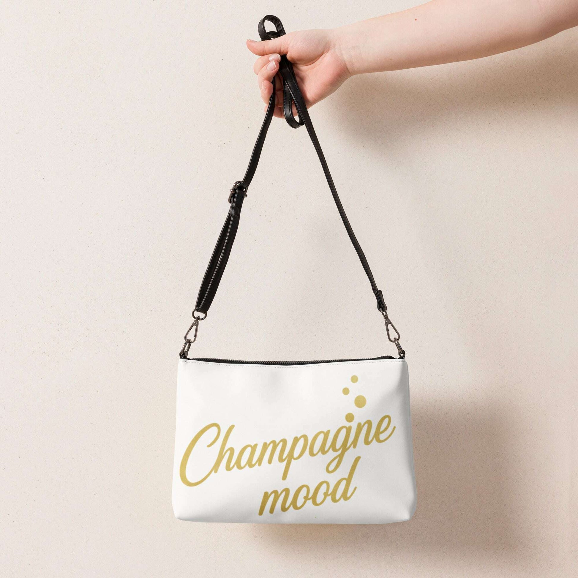 White cushion with gold Champagne Mood text held by hand with black strap, chic accessory for wedding weekend decor and bridal celebration