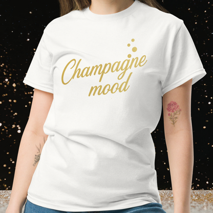 Woman wearing white Champagne Mood t-shirt with gold lettering on festive background, chic white and gold outfit for bridal shower, bachelorette party or celebration