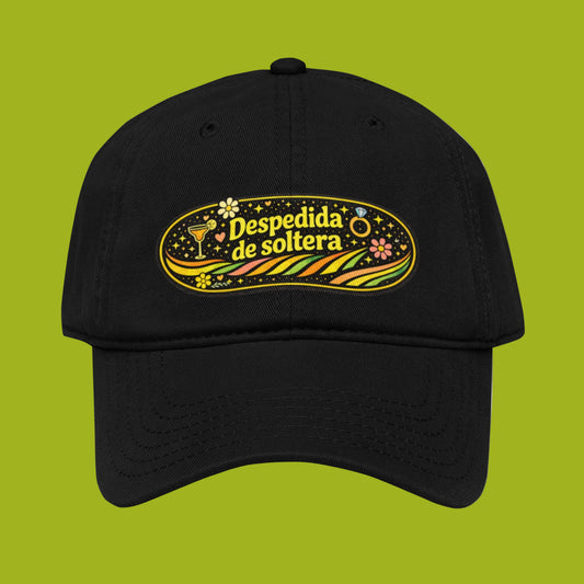 Vista frontal de gorra negra con diseño ovalado “Despedida de soltera” en tonos amarillo y verde sobre fondo verde lima.