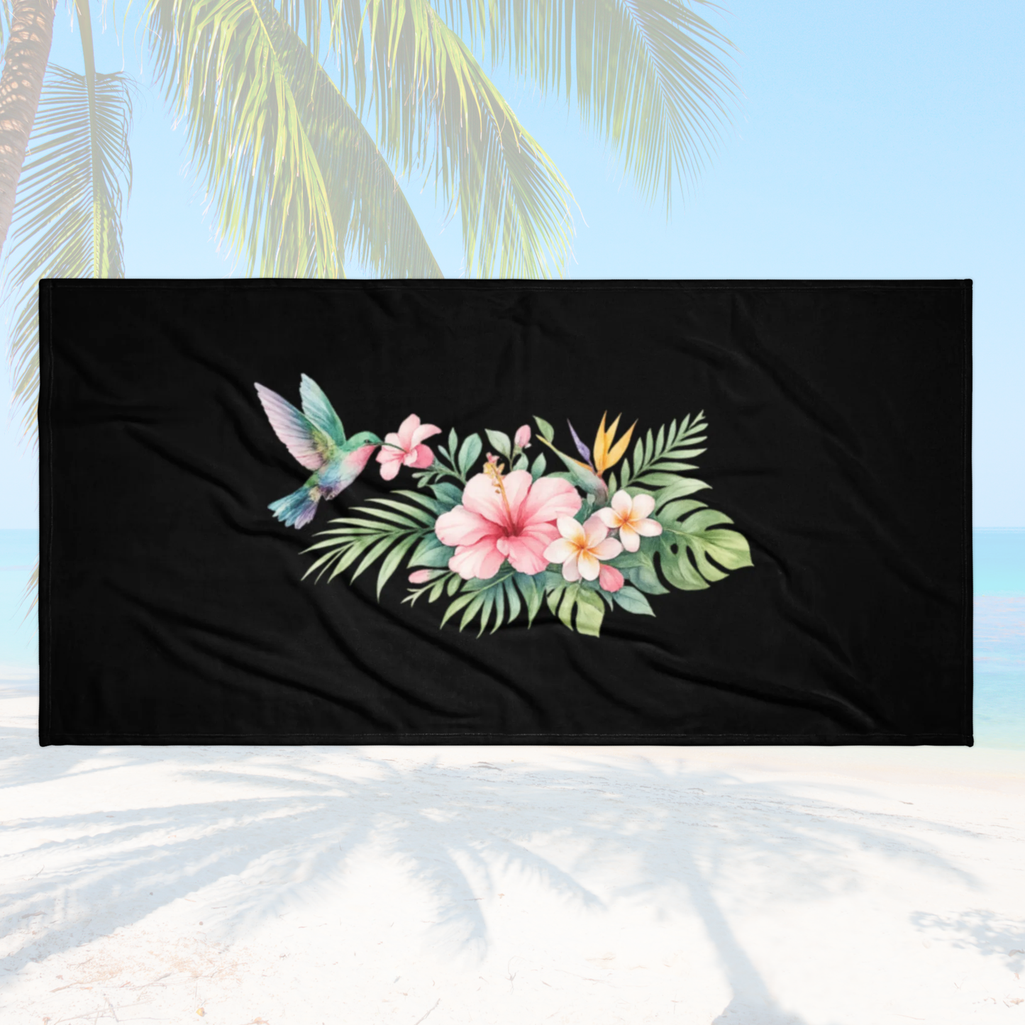 Serviette noire motif fleurs tropicales et colibri posée sur décor plage pour enterrement de vie de jeune fille.