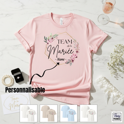 T-shirt rose personnalisable “Team de la Mariée – Name” avec couronne florale délicate et forme géométrique dorée, présenté en mise en scène EVJF avec bague, coupe de champagne et accessoires de mariée.
