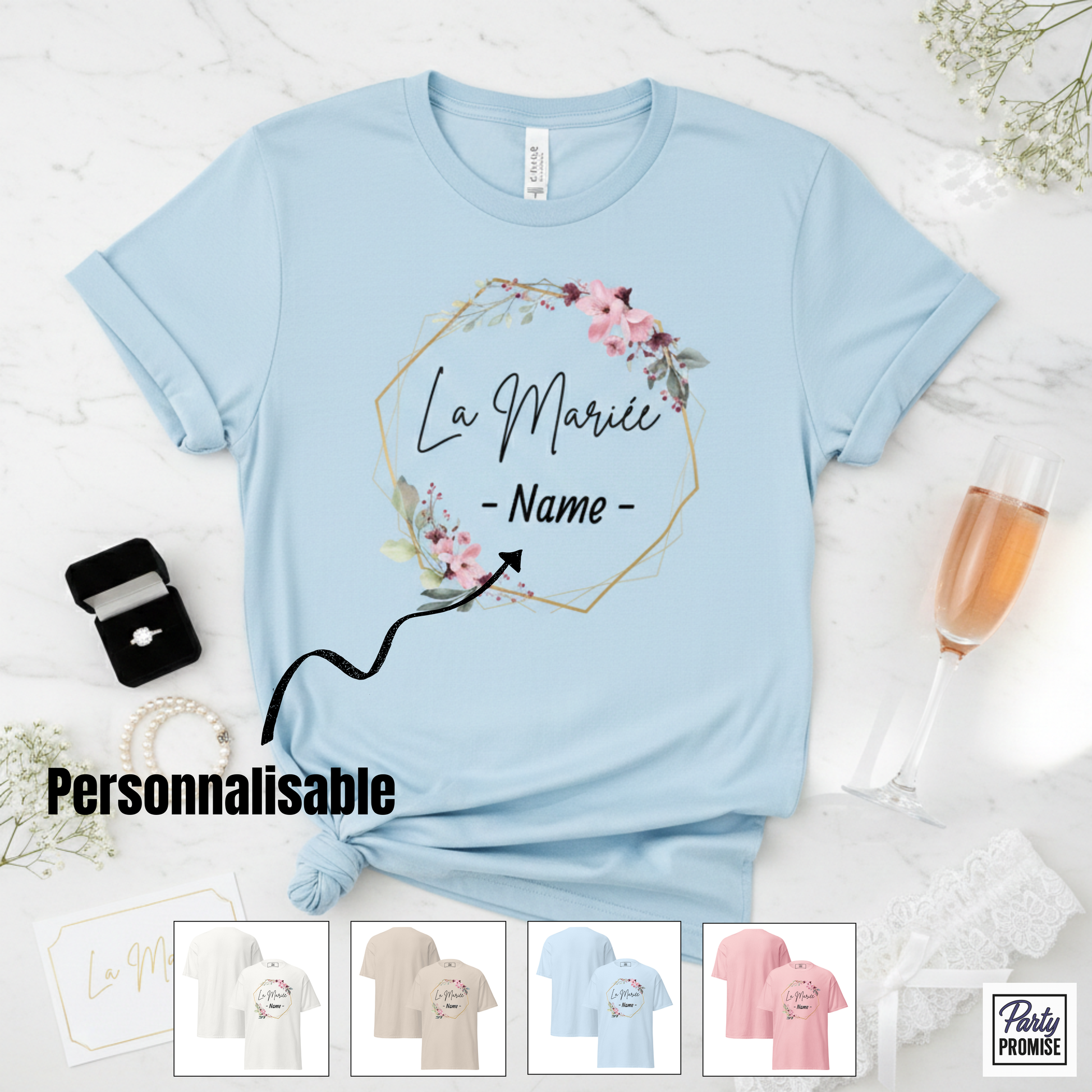 T-shirt bleu pastel personnalisable “La Mariée” avec cadre floral et prénom au choix, posé sur fond marbre avec bague, coupe de champagne et accessoires EVJF, collection Party Promise.