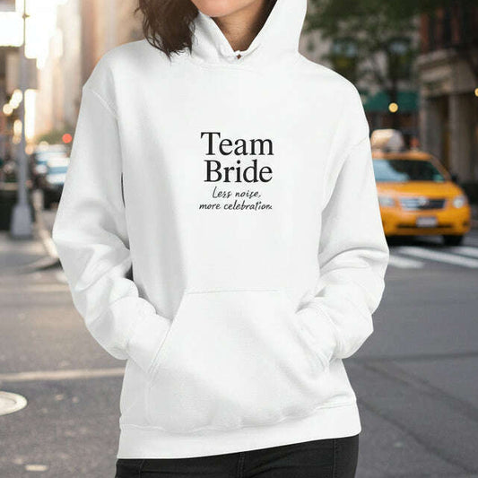 Woman wearing white hoodie with minimalist “Team Bride” black lettering, chic outfit for bachelorette party, bridal squad or girls weekend.