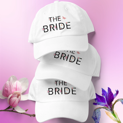 Stack of white embroidered The Bride caps with floral accents, ideal accessory for bride during wedding weekend or bachelorette party.