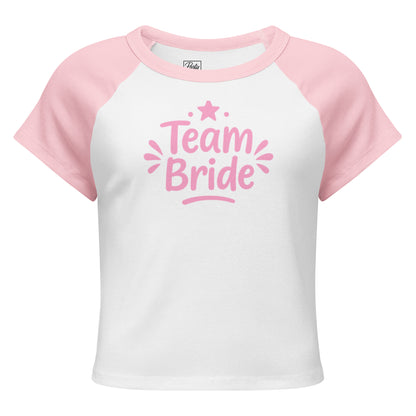 White and pink raglan “Team Bride” t-shirt laid on a clean white background. The contrast sleeves and soft ribbed texture highlight its sporty and feminine style.