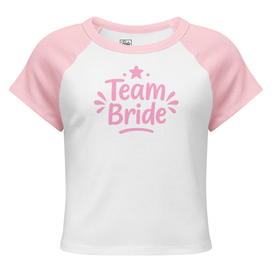 White and pink raglan “Team Bride” t-shirt laid on a clean white background. The contrast sleeves and soft ribbed texture highlight its sporty and feminine style.