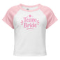 White and pink raglan “Team Bride” t-shirt laid on a clean white background. The contrast sleeves and soft ribbed texture highlight its sporty and feminine style.